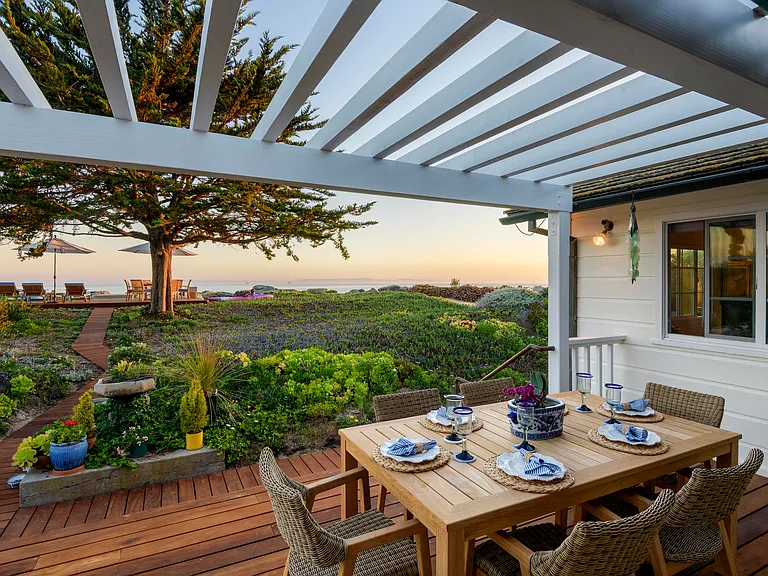 View out the back door showing brand new back deck with copper railings to walk down a few steps to walkway to oceanfront deck. New pergola and new 6 seating table and chairs.
