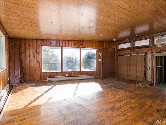 View of living room from kitchen.  Large windows allow for lots of light and have storm windows.  Additional paneling left in left corner.  Two steps down on right takes you to 2 bedrooms and bath area.  Original hardwood floors.