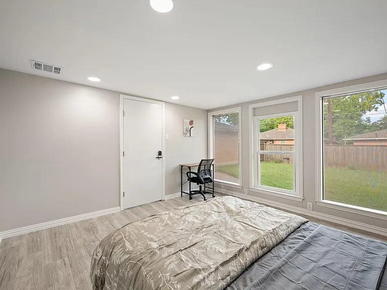 Bedroom with large corner windows, wood-look flooring, and space for a bed plus a small work area.