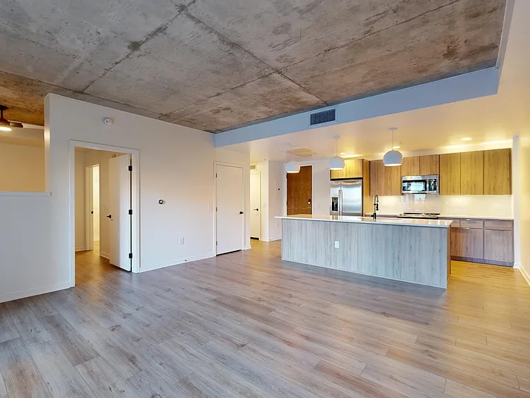 Apartment kitchen with stainless steel appliances, dining and living room with wood-style flooring.