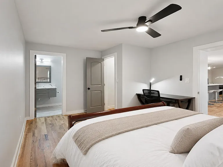 Spacious furnished bedroom with hardwood floors, ceiling fan, and a dedicated desk area, plus convenient access to kitchen.