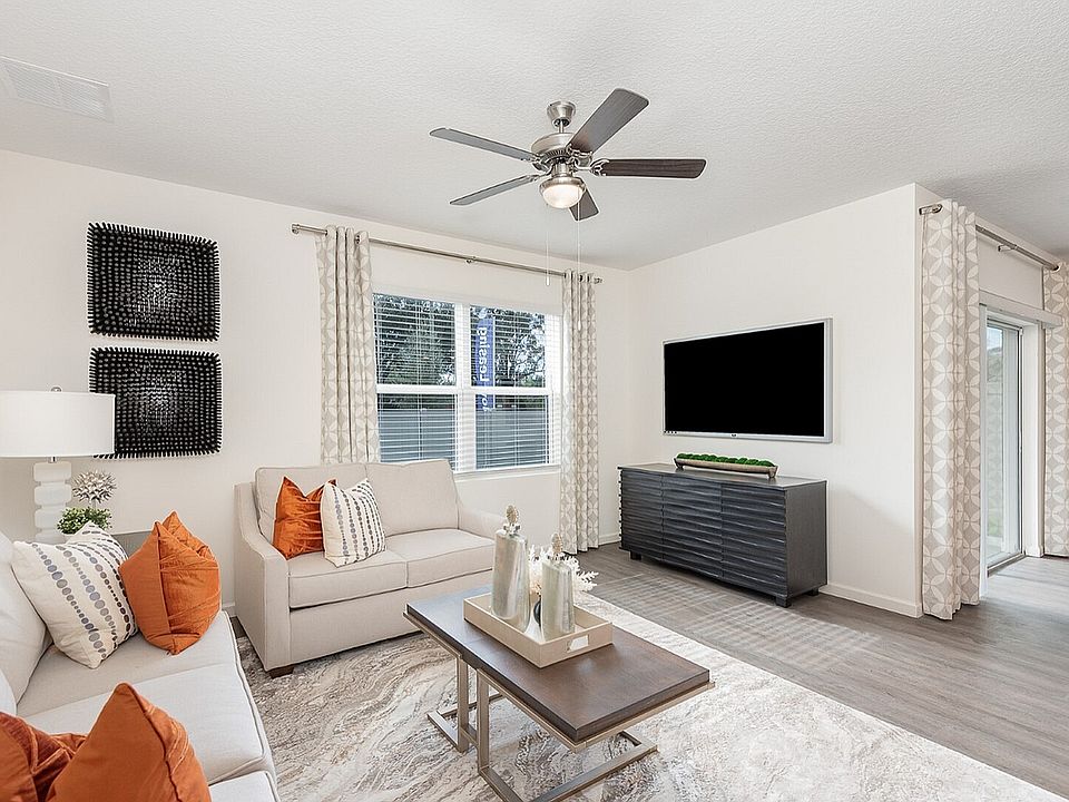 Bright and modern living room featuring sleek decor, plush seating with vibrant pillows, and a large wall-mounted television, perfect for relaxation and entertaining.