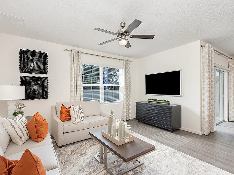 Bright and modern living room featuring sleek decor, plush seating with vibrant pillows, and a large wall-mounted television, perfect for relaxation and entertaining.
