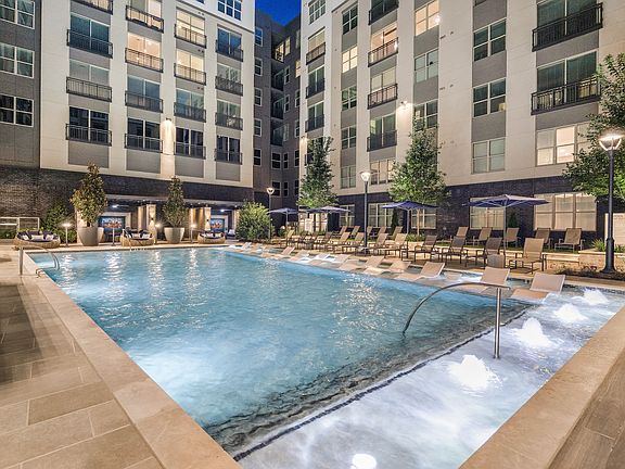 Luxurious apartment complex with a beautifully illuminated pool, surrounded by modern architecture and lush greenery, perfect for a relaxing evening swim.