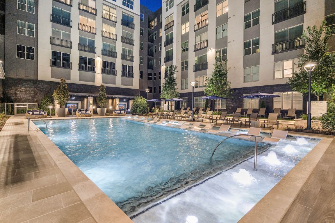 Luxurious apartment complex with a beautifully illuminated pool, surrounded by modern architecture and lush greenery, perfect for a relaxing evening swim.