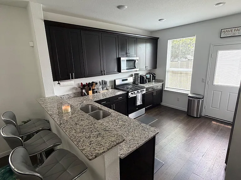 Kitchen with dark cabinetry, granite peninsula seating, stainless appliances, and a window for natural light.