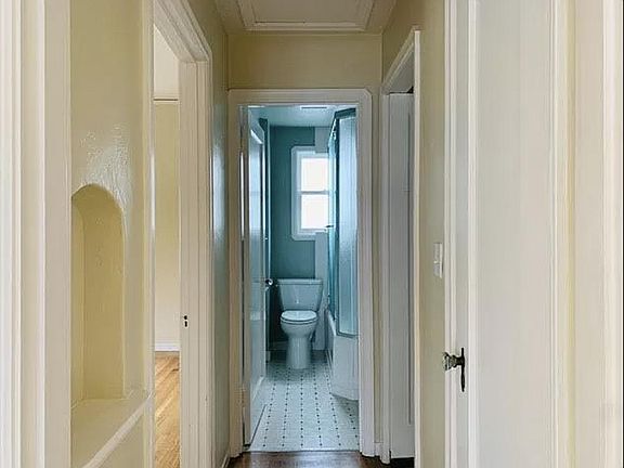 Hallway to the bathroom, bedroom (left), and kitchen (right) with a small nook for keys and decor (left) and a linen closet (right)