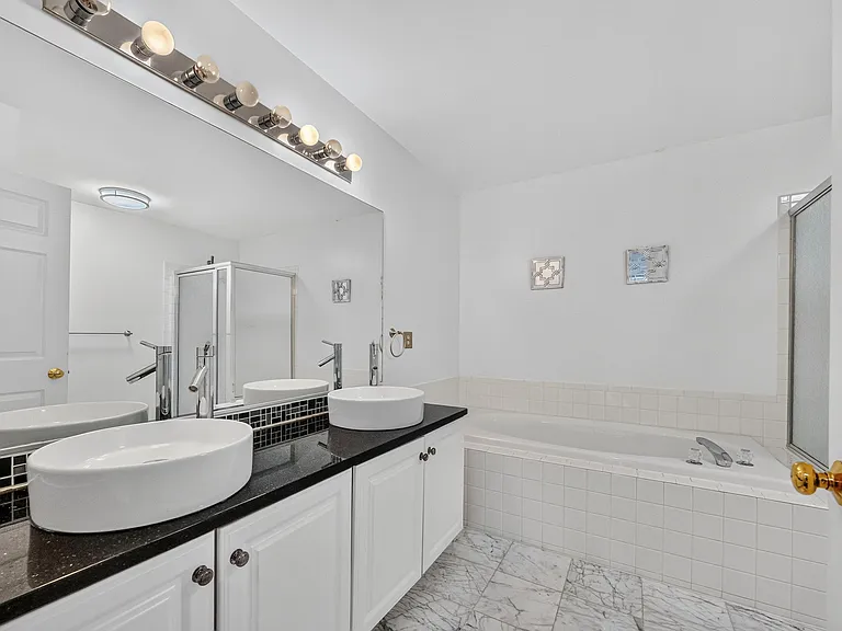 Spa-like Primary Bath with dual sinks, dark granite counters, a soaking tub, glass enclosed shower, and marble tile.
