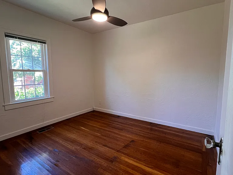 Second bedroom with ceiling fan, closet, hardwood floors, and window with a lovely view of backyard.