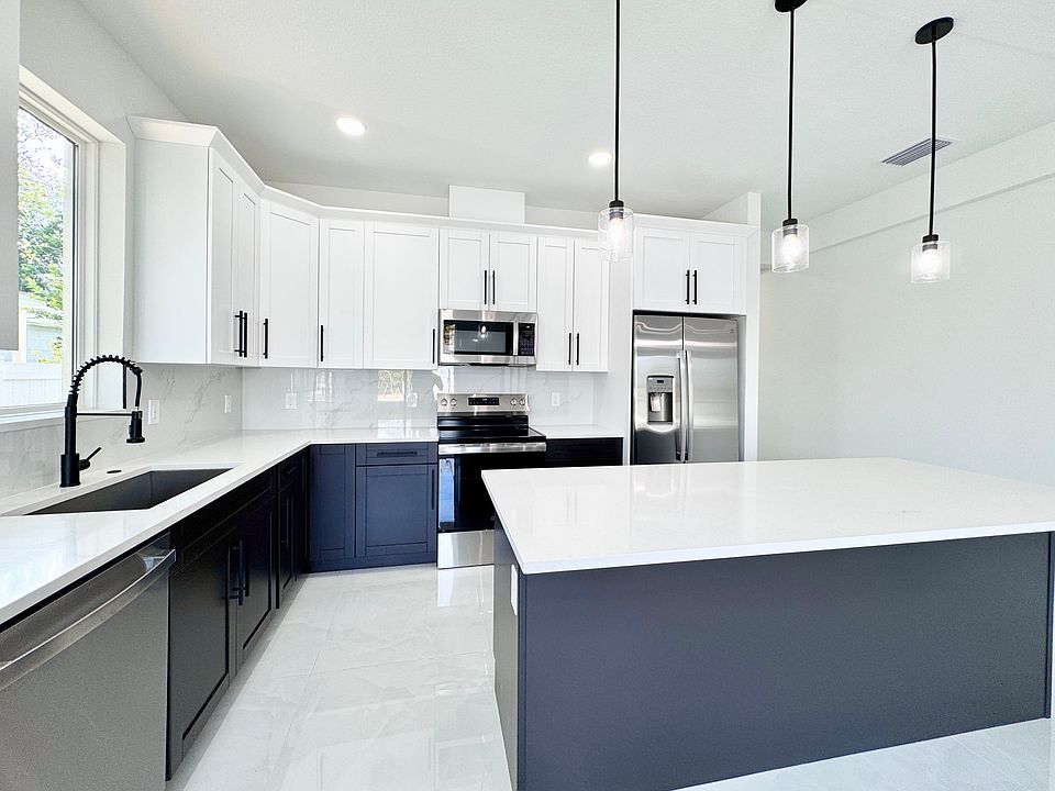 The spacious open kitchen features quartz countertops, stainless steel appliances, soft-close cabinets, a large island, and modern pendant lighting.