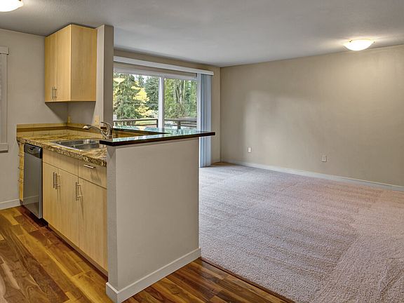 A kitchen with stainless steel appliances, stone countertaps, a small breakfast bar, and a view into the living area