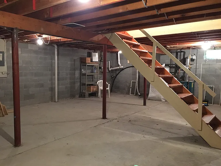 Unfinished basement with boiler and hot water tank behind stairs