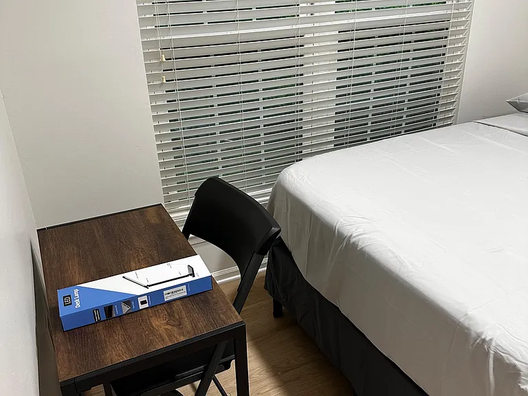 Bedroom setup with a furnished work desk, chair, and window blinds for privacy and light control.