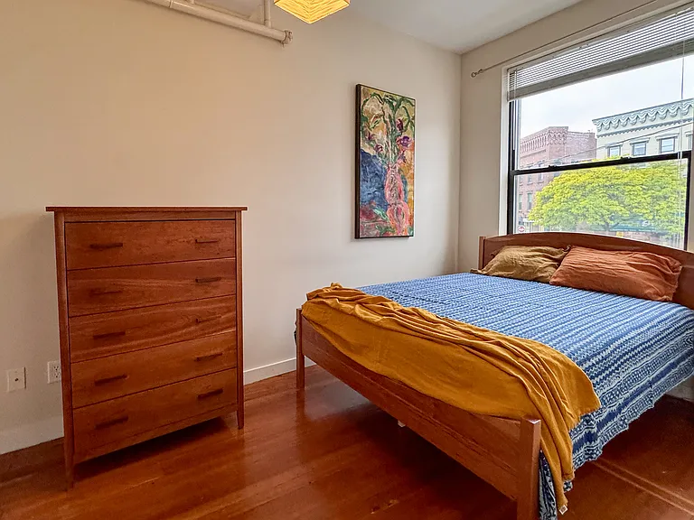 Primary bedroom with queen size cherry frame bedframe and cherry wood dresser.