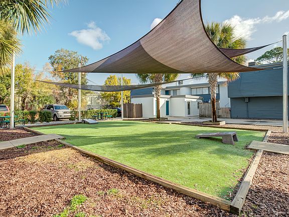 Inviting outdoor common area with modern shade sails, lush green lawn, and picnic tables amidst palm trees, perfect for relaxation and social gatherings.