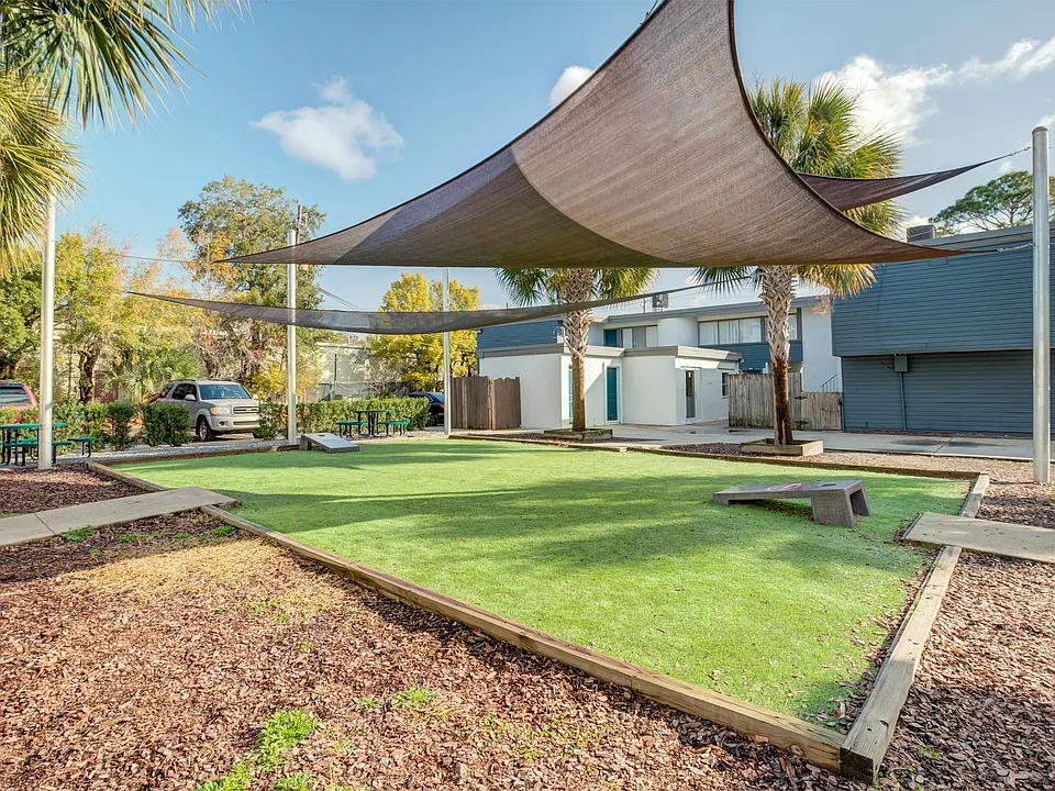 Inviting outdoor common area with modern shade sails, lush green lawn, and picnic tables amidst palm trees, perfect for relaxation and social gatherings.