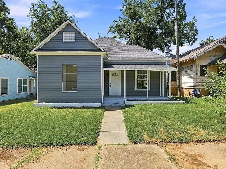 Updated front exterior with attractive gray siding, white trim, a covered front porch, newer composition roof, mature trees, large windows, and excellent curb appeal. A welcoming entrance creates an inviting first impression.