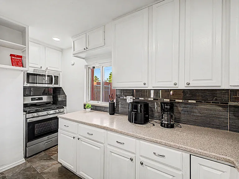 Functional kitchen with ample white cabinetry, long prep counter, gas range, and a window over the workspace.