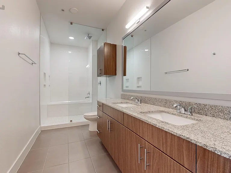 Apartment bathroom with large soaking tub, glass-enclosed shower, wood-style flooring, and double sinks.