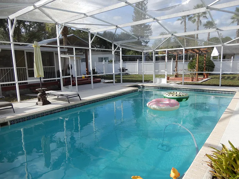 View from south end of pool showing pergola, gazebo, screened porch and 6 ft+ PVC fencing around entire backyard.