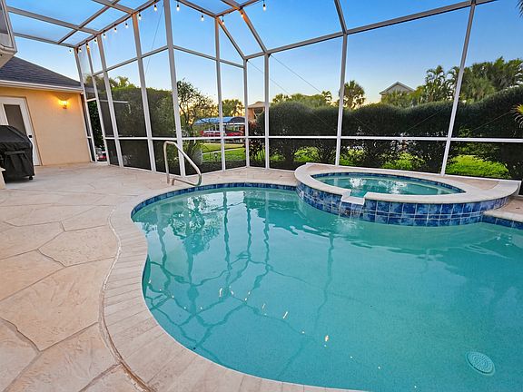Pool View from Lanai looking out across saltwater canal. Pool bathroom is just past the natural gas hooked-up stainless weber grill that is covered (included). Outdoor Shower is in the back corner just outside the enclosed pool cage, in a private area.