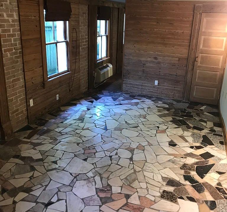 Living room with broken marble floor, exposed brick, wood walls and air/heat unit.