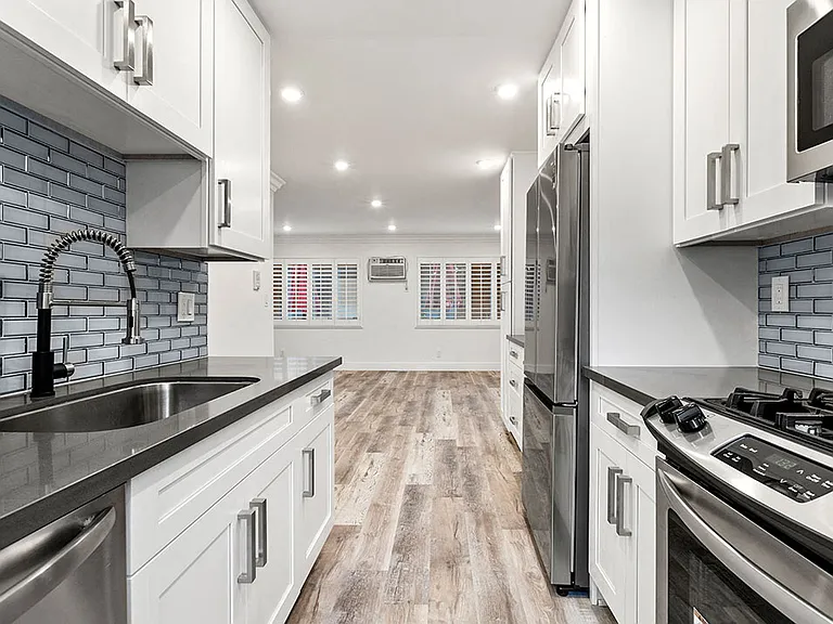 Glass tiled kitchen with stainless steel appliances and view of spacious living room.