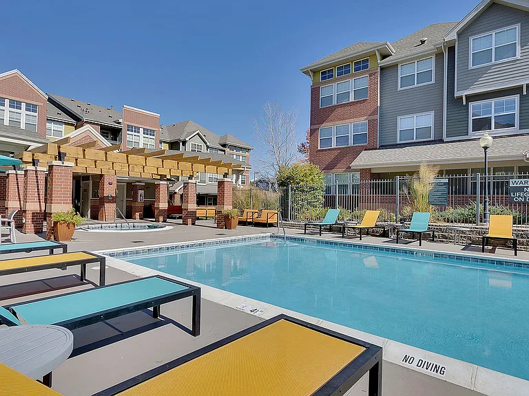 Inviting apartment community pool area with sun loungers, blue sky backdrop, and modern brick buildings.