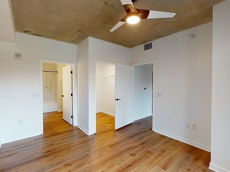 Spacious apartment bedroom with large closet, attached bathroom and wood-style flooring.