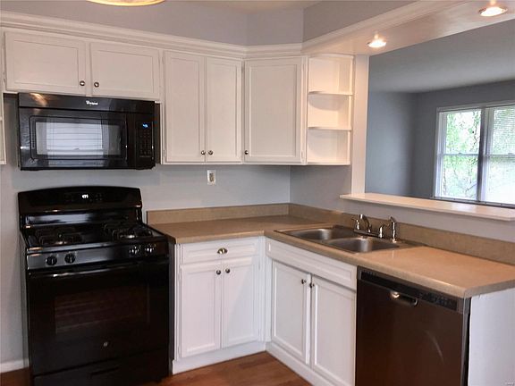 Southeast facing view of kitchen shows dishwasher, sink, stove, microwave and pass through to sunny living room windows.