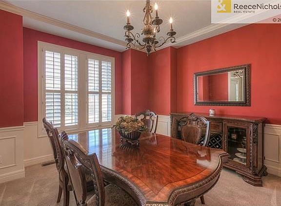 A formal dining room has wainscoting below and plantation shutters.
