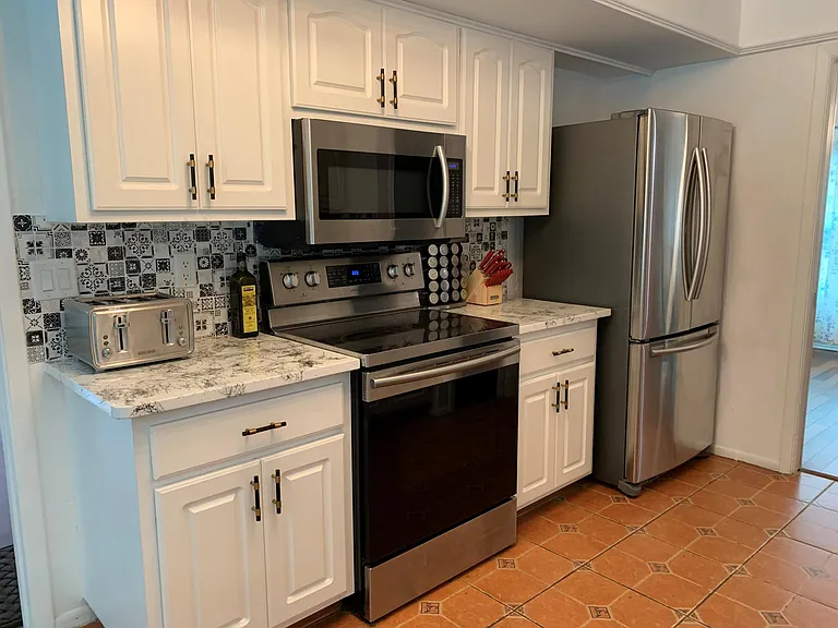 The other side of the kitchen with a microwave oven, an electric range with a glass top and a full size oven, a fridge, a toaster, counter and cabinets, which is full of items needed in the kitchen.