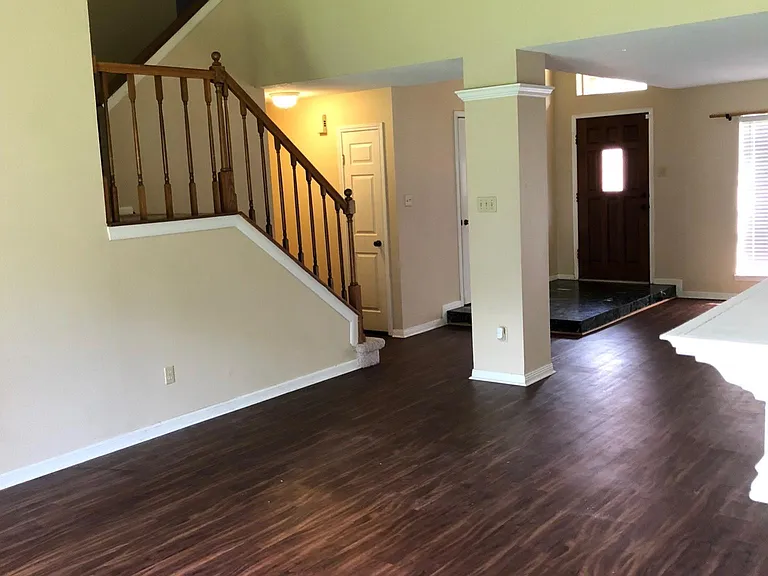 Now camera man standing in living room, looking at entry way, dining room and stairs to upstairs bedrooms and bonus living room