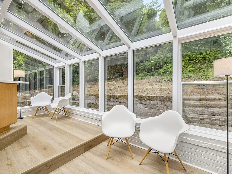 Sunroom with floor-to-ceiling windows and a glass ceiling, offering a spacious sitting area with wooded views.