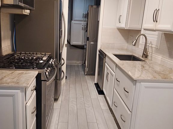 Galley kitchen and the adjacent utility room. Modern stainless-steel applances, marble backsplash, porcelain countertops, and wood cabinets complement the luxury vinyl planking on the floor.