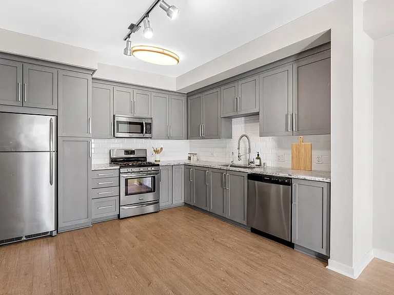 Kitchens with grey cabinetry, grey speckled granite countertops, white subway tile backsplash, stainless steel appliances, and hard surface flooring