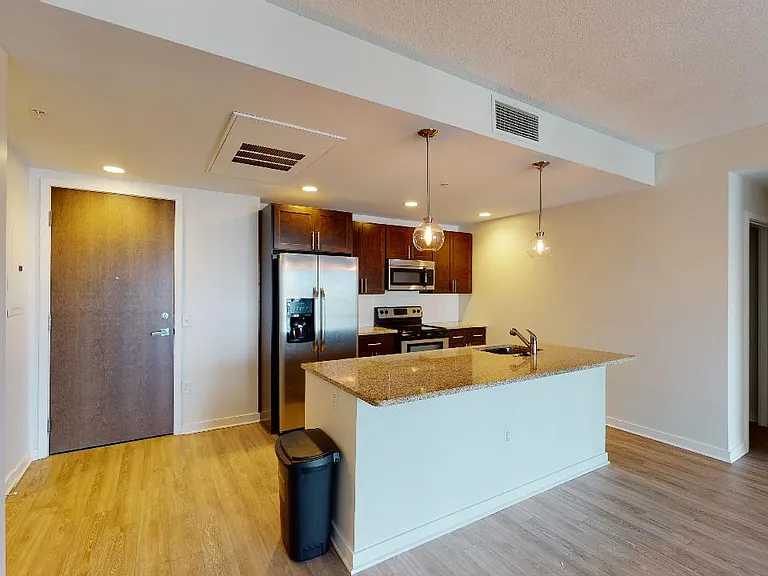 Apartment kitchen with stainless steel appliances, granite countertops and wood-style flooring.