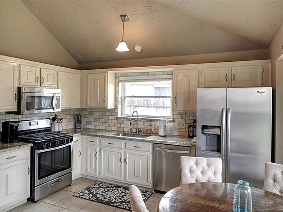 Kitchen with granite countertops and stainless steel appliances, high ceiling.