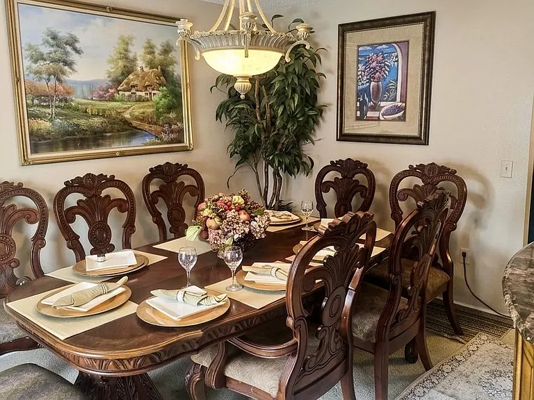 Formal dining area with a large carved wood table, seating for eight, and an overhead chandelierideal for shared meals.