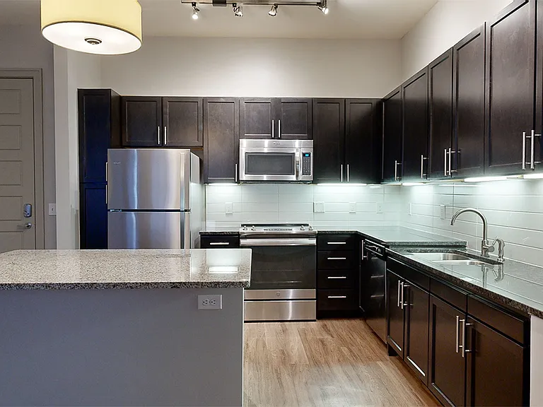 Apartment kitchen with stainless steel appliances, wood-style flooring, and granite countertop island (shown here). Kitchen peninsula available in select homes.