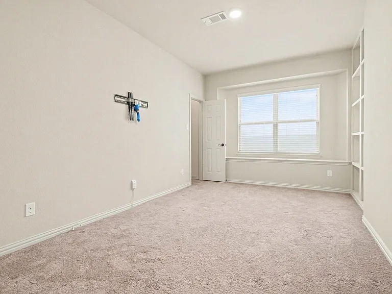 Carpeted room featuring a large window with horizontal blinds, built-in shelving, neutral wall paint, and white trim