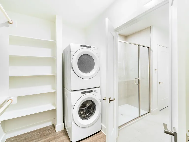 In-home laundry with stacked washer and dryer inside the primary closet features open shelving for efficient daily routines.