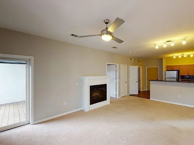 Apartment kitchen, dining and living room with plush carpet flooring.