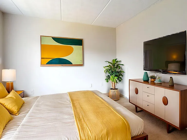 Inviting bedroom with vibrant yellow accents, chic decor, wall-mounted TV, and a modern dresser, designed for cozy relaxation.