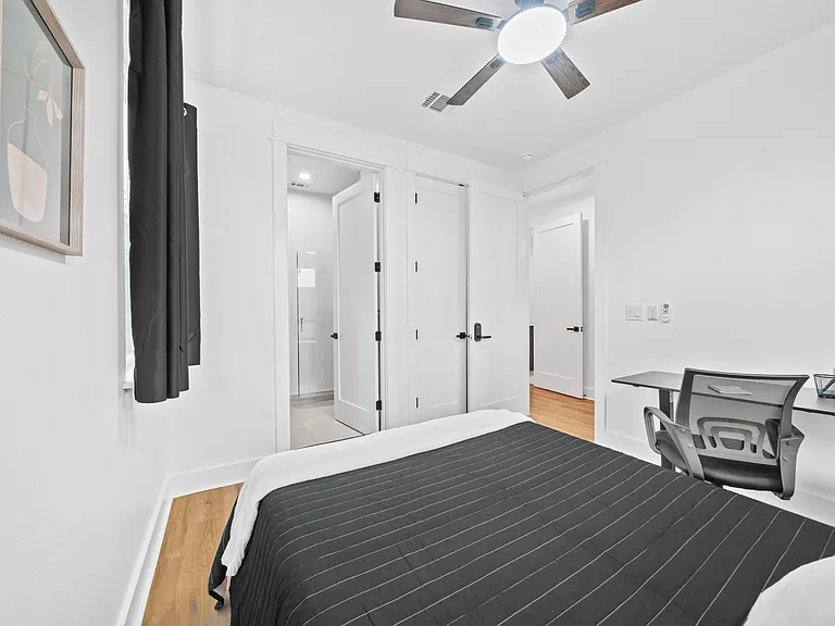 Private bedroom featuring a ceiling fan, hardwood floors, and an in-room desk plus closet and nearby bathroom access.