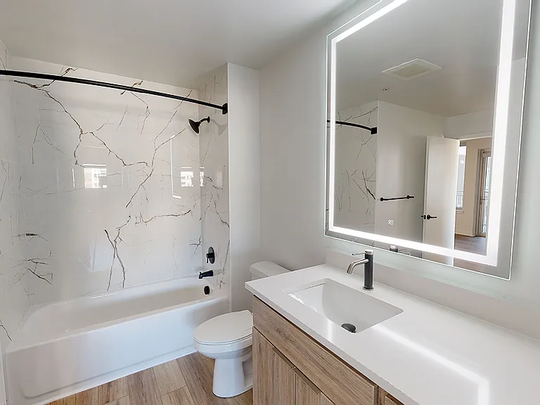 Apartment bathroom with wood-style flooring and LED vanity mirror.