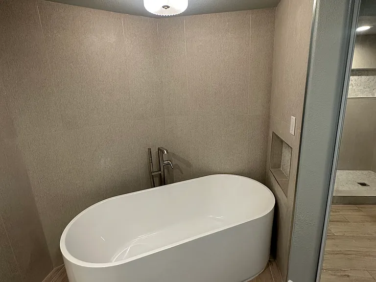 Brand new primary bathroom showing freestanding tub, Kohler fixtures, second closet behind mirror on the right.