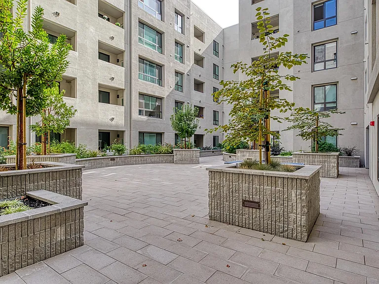 Paved courtyard with raised planters, greenery, and firepits that create a calm outdoor space.