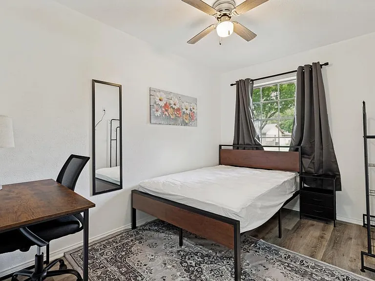 Furnished bedroom with a full bed, work desk, and Wardrobe, plus a window with curtains, TV and ceiling fan.