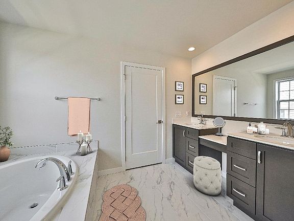Master bath with double vanity sink, large soaking tub, and frameless shower door